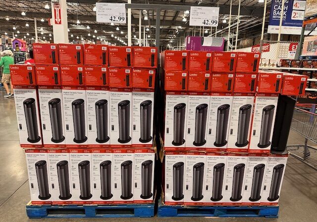 Stacked boxes of Lasko Digital Ceramic Tower Heaters are displayed on pallets in a warehouse store; price signs above show $42.99.