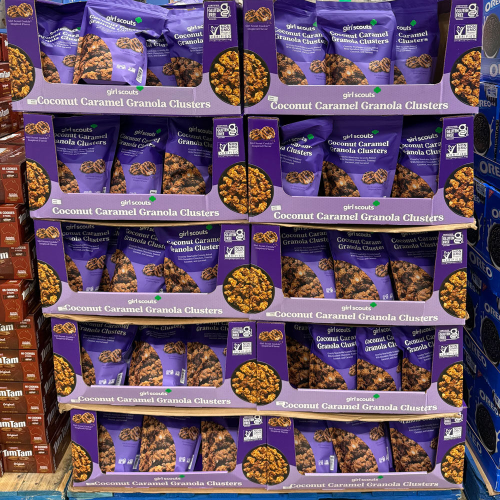 Display of stacked boxes containing Girl Scouts Coconut Caramel Granola Clusters in purple packaging on a store shelf.