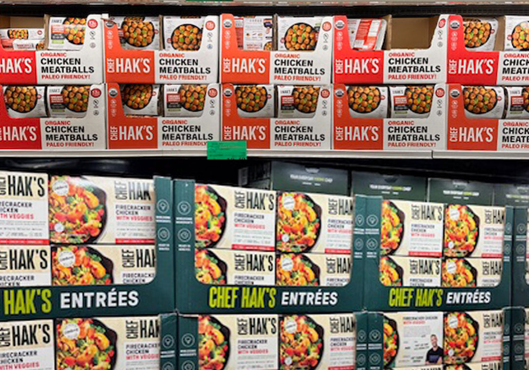 Shelves stocked with boxes of Hak’s Organic Chicken Meatballs and Chef Hak’s Entrées, arranged in rows at a grocery store.